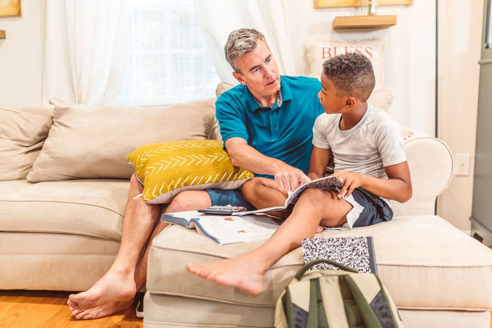 An older volunteer talks through a workbook with a pre-teen boy on a living-room couch